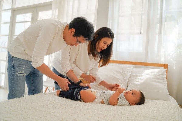 Young Asian couple helping one another to change their baby’s diaper.