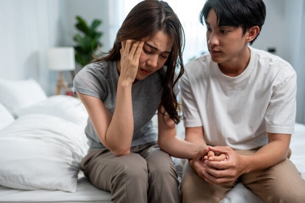  An Asian man comforting his sad wife in their bedroom.