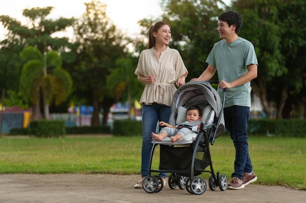 A young Asian couple talking and pushing their baby in the stroller for a walk in the park at dusk.