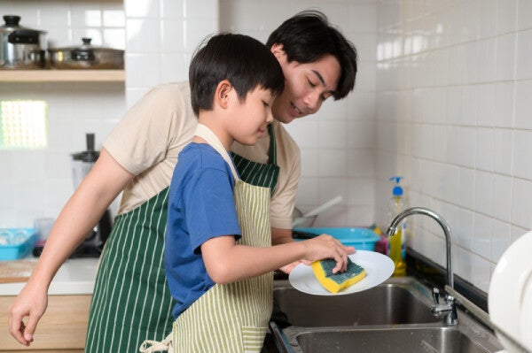 Asian father and son washing dishes together.