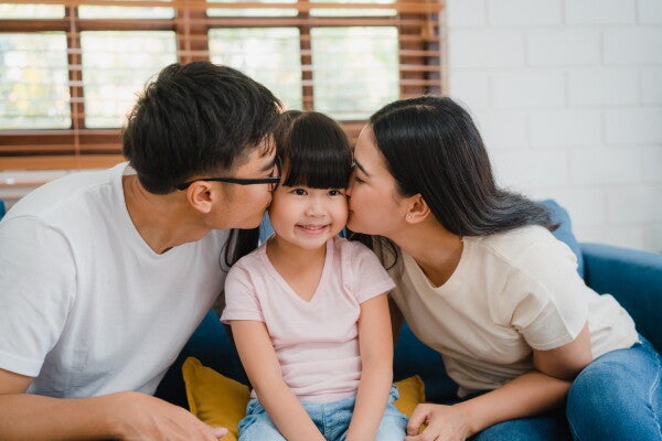 A young Asian couple kissing their little girl whose sitting in between them.