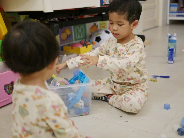 Two Asian kids putting away their toys before bedtime to help tidy up.