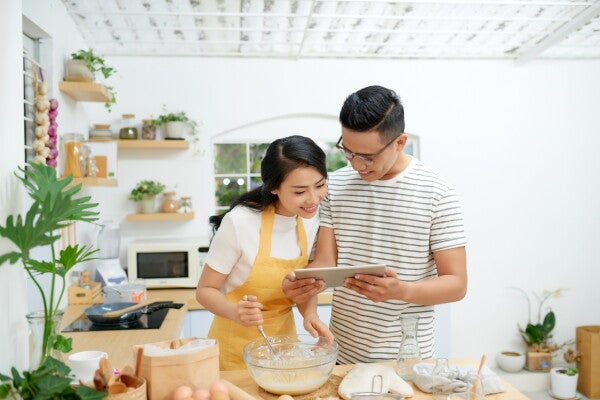 Asian man and woman cooking at home, looking at a recipe.