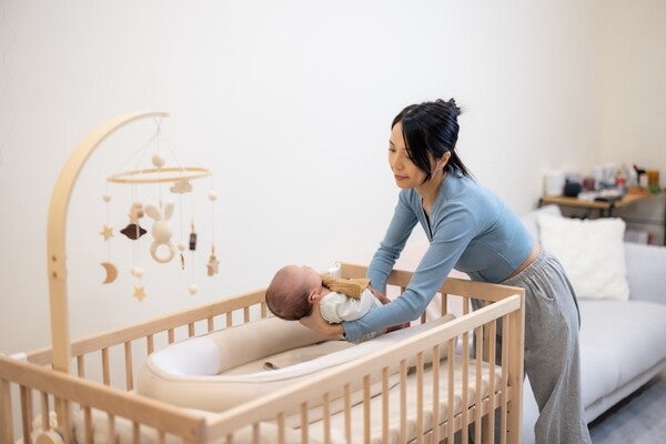 Asian mom putting her baby down into the crib