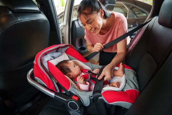 A young Asian mom securely fastening her baby into a rear-facing car seat. 