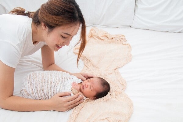 Asian mom swaddling her baby in bed