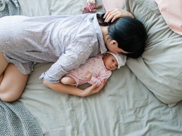 A young Asian mother sleeping with her newborn baby during the day.