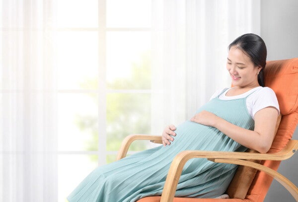 Young pregnant Asian woman resting in a rocking chair at home.
