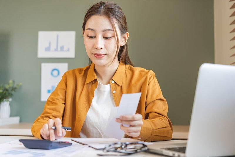 Young Asian female working abroad calculates her budget and adjusts her financial plan.