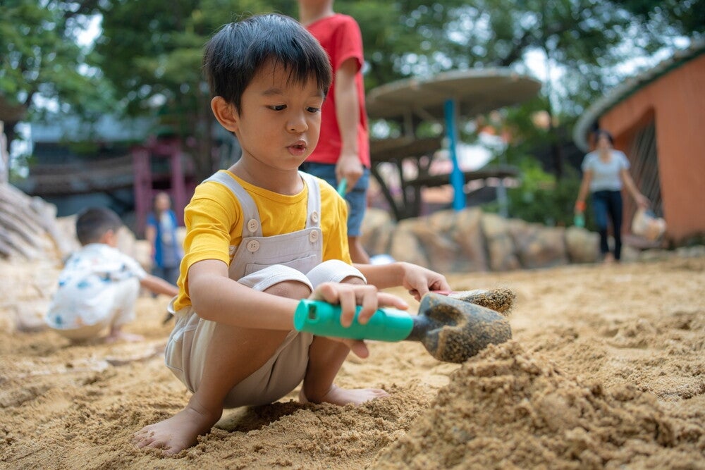 Young Asian male child plays using a shovel plays on a sand box.