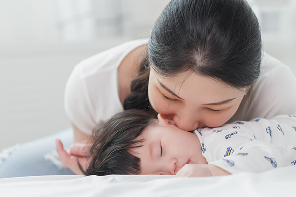 Young Asian mom kisses her son as he finally falls asleep