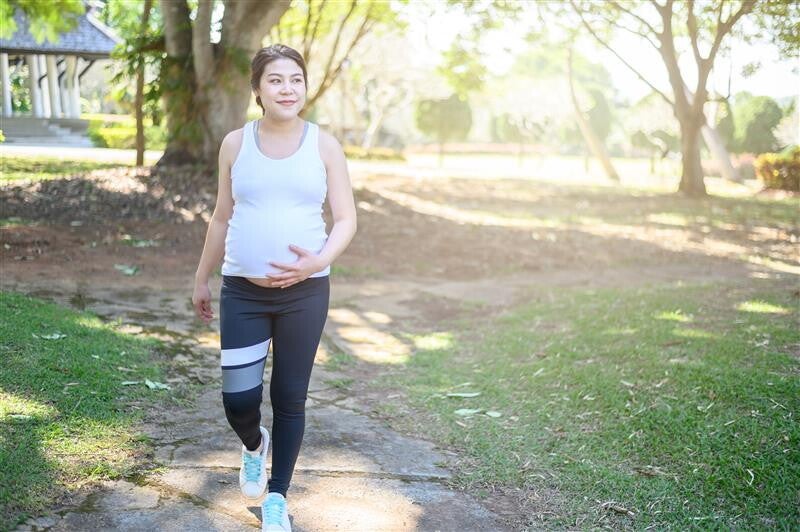 Young Asian pregnant woman cools down after brisk walking at a park.