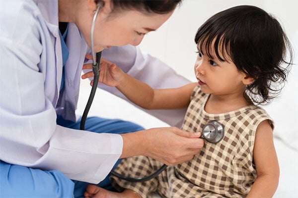 Young Asian toddler holds the doctor's stethoscope during a checkup for signs of low calcium.