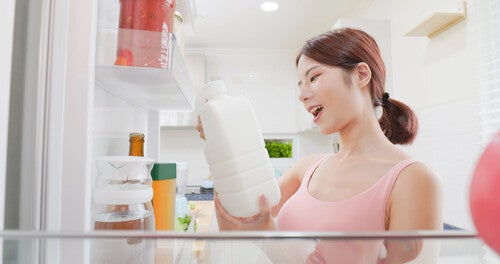 Young Asian woman getting a milk bottle out of the fridge and checking its expiration date