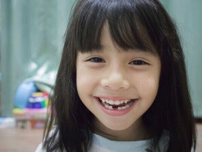 A little Asian girl smiling widely to show her teeth, which have a gap at the bottom.