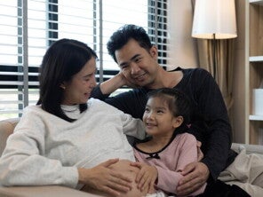 A pregnant woman and her husband with their stepdaughter on a couch, happy as a blended family.