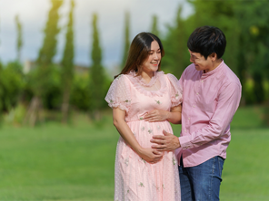 A woman who is 15 weeks pregnant cradles her baby bump as she and her husband walk in the park.