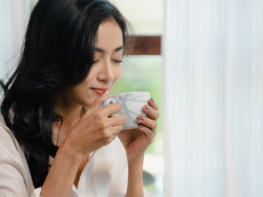 A young Asian woman enjoys a cup of coffee beside the window as part of her morning routine