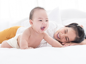 An Asian mother watching her smiling 6-month-old baby trying to crawl on the bed