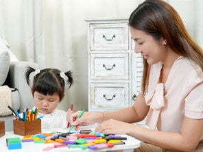 A young Asian mom teaching her little girl to color—one of the fun activities for kids at home to keep them busy.
