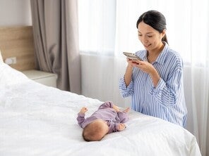 Asian mom getting a clear baby picture of her little one lying on a white bed overhead.
