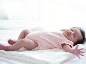An Asian newborn girl is startled while asleep, triggering the Moro reflex, jerking arms outwards. 