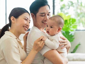 Asian dad with his wife behind him carries their healthy baby in his arms. Asian dad with his wife behind him carries their healthy baby in his arms.