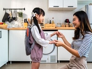 Asian mom holding little girl’s hand in the kitchen after giving her baon bag with milk products for school