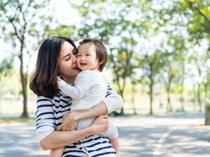 Asian mom kisses her toddler while carrying her in her arms during a walk in a park Asian mom kisses her toddler while carrying her in her arms during a walk in a park