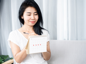 Asian woman checking the calendar for ovulation or menstruation to understand PMS symptoms vs pregnancy symptoms