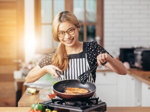 Asian woman frying fish in a pan in her kitchen