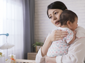 Asian young woman burps her baby over her shoulder after feeding. 