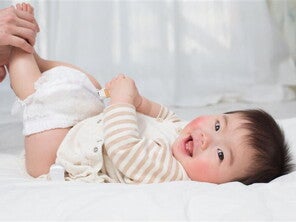 Hands holding a smiling Asian baby’s legs and removing the diaper to check baby poop color. 