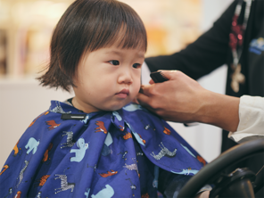 Little Asian girl getting a toddler haircut at a kid’s salon.