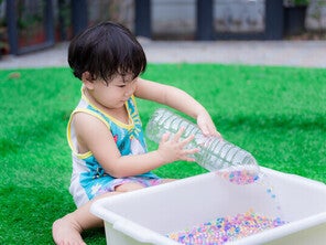 Little Asian boy playing with a DIY Montessori toy, like an empty plastic bottle and beads in a container