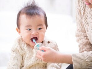 Cropped pic of mom’s hand brushing her infant’s teeth with baby toothpaste.