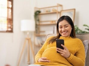Pregnant Asian woman using her phone to message her ob-gyne for her birth plan.
