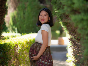 Smiling pregnant Asian woman wearing a cotton dress outdoors and showing off her baby bump.