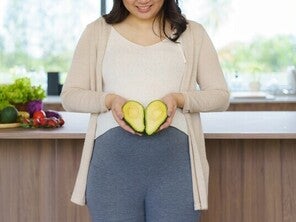 Pregnant Asian woman holding a sliced avocado—one of the best fruits for pregnant women