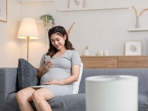 Pregnant Asian woman on a sofa looking at her pregnancy app on her phone at home