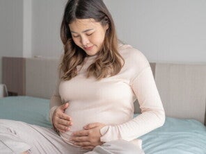 Pregnant Asian young woman who is 32 weeks pregnant stares at her baby bump 