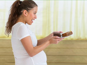 Pregnant woman holding plate with two pieces of cake