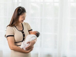 A new mom holding her newborn baby while standing at home, happy with her self-care plan.