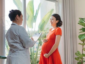 Happy Asian pregnant woman in red talking to doctor.