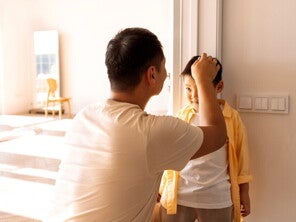 Asian dad marks his son's height on the wall to record growth milestone. Asian dad marks his son's height on the wall to record growth milestone.