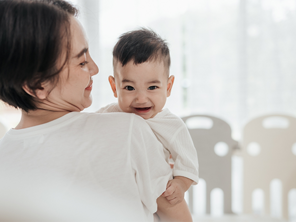 Smiling Asian mom with her laughing baby enjoys the early childhood stage
