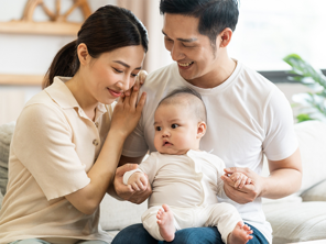 Smiling mother and father holding newborn son at home, considering birth control methods for family planning