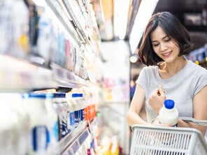 Young Asian woman putting a milk bottle in her basket after choosing from the types of milk in the supermarket