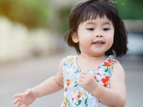 Asian female toddler runs in the street during summertime.