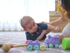 A young Asian woman playing with a baby boy on the floor using educational toys.